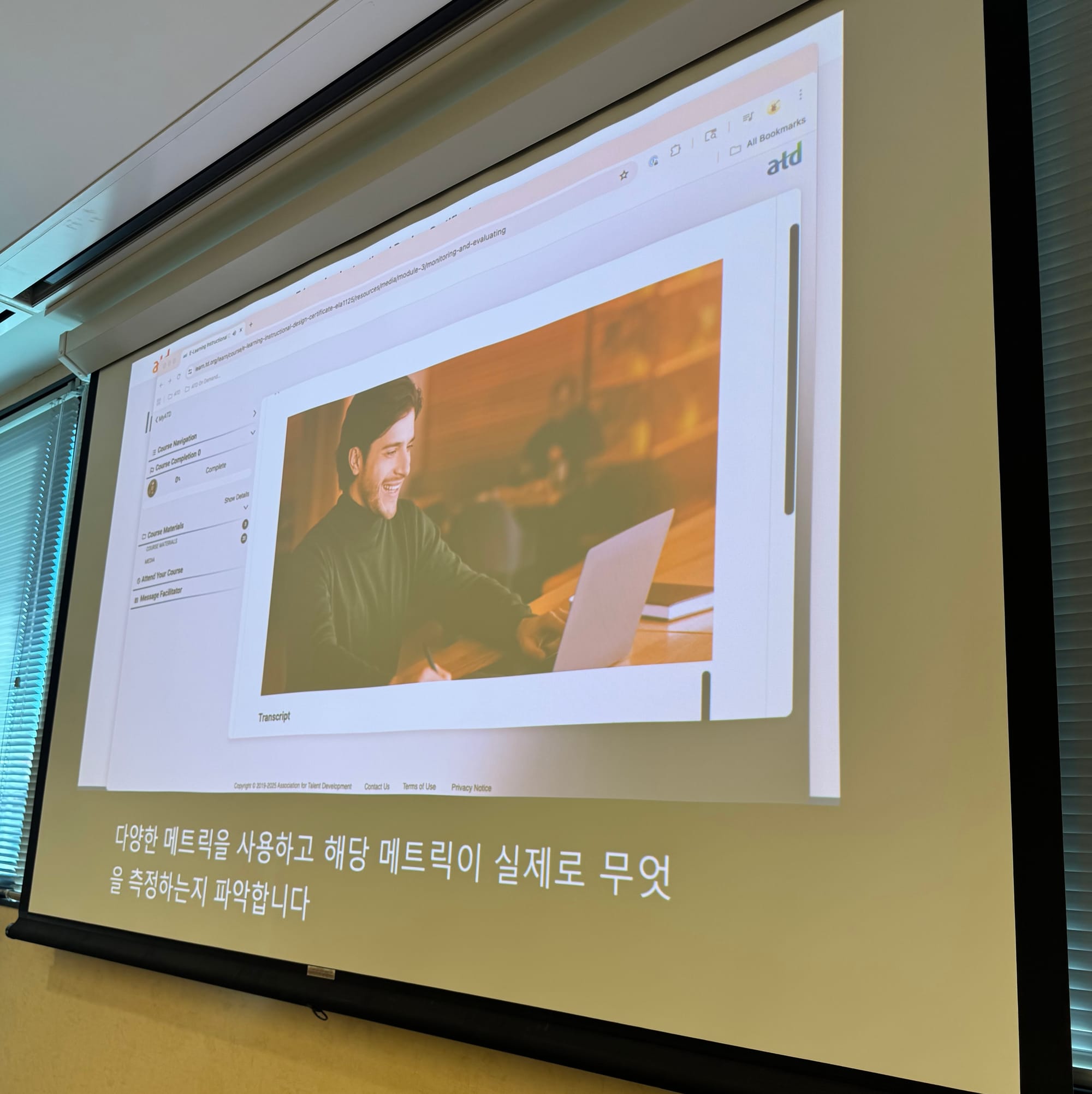 A projected screen in a classroom with an e-learning course interface. PowerPoint is also open with Korean subtitles.